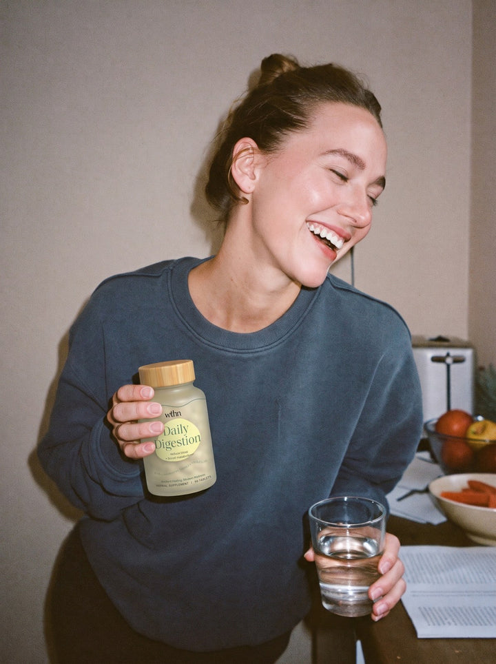 Laughing in the kitchen with a bottle of Daily Digestion and a glass of water