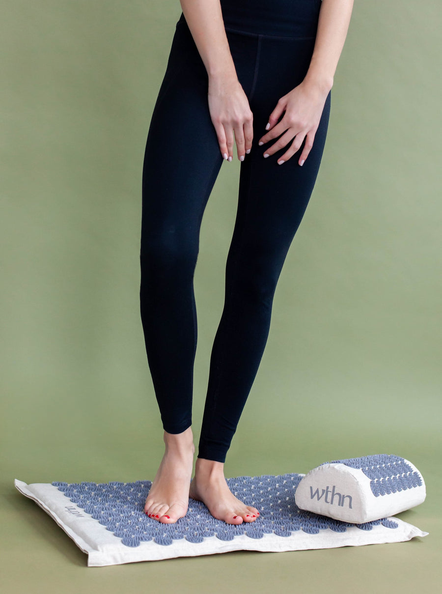 Bare feet standing on the WTHN acupressure mat, the pillow beside them