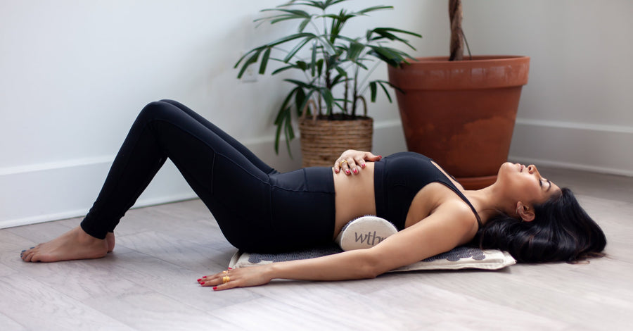 A woman resting on the WTHN acupressure mat on a living room floor, the pillow under her lower back