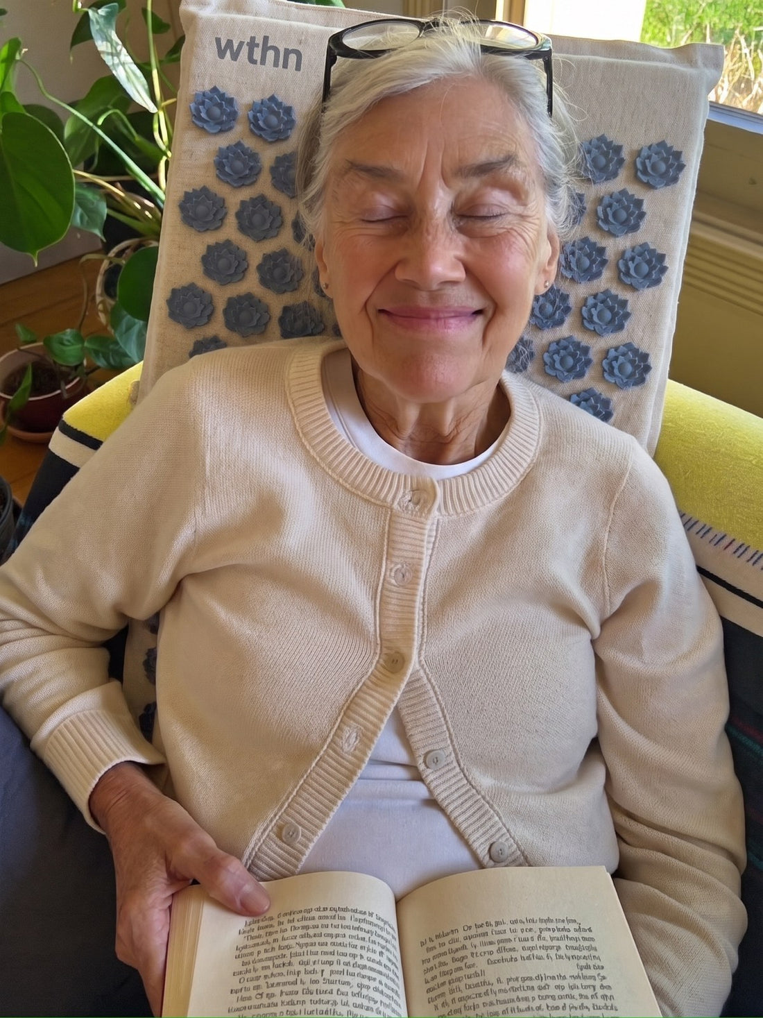 An older woman reading on the sofa with the WTHN acupressure mat behind her back