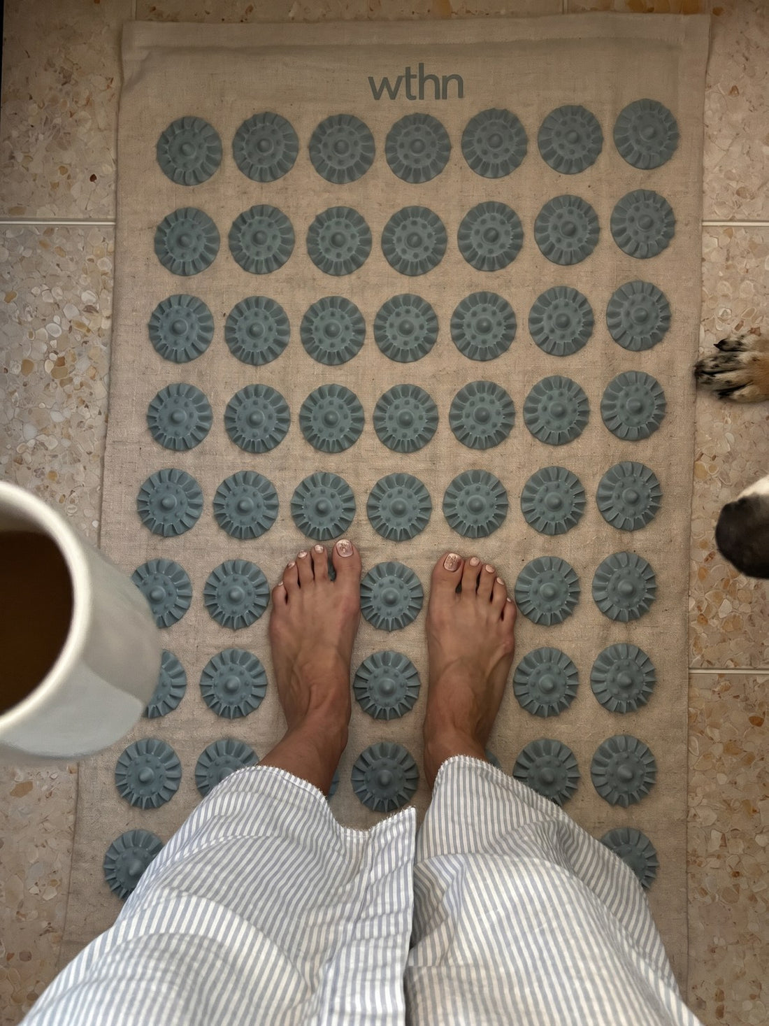 Bare feet on the WTHN acupressure mat on a kitchen floor next to a cup of coffee